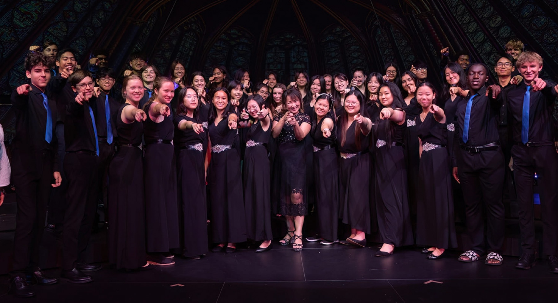 The choir on stage with Joyce Goh, pointing at the camera